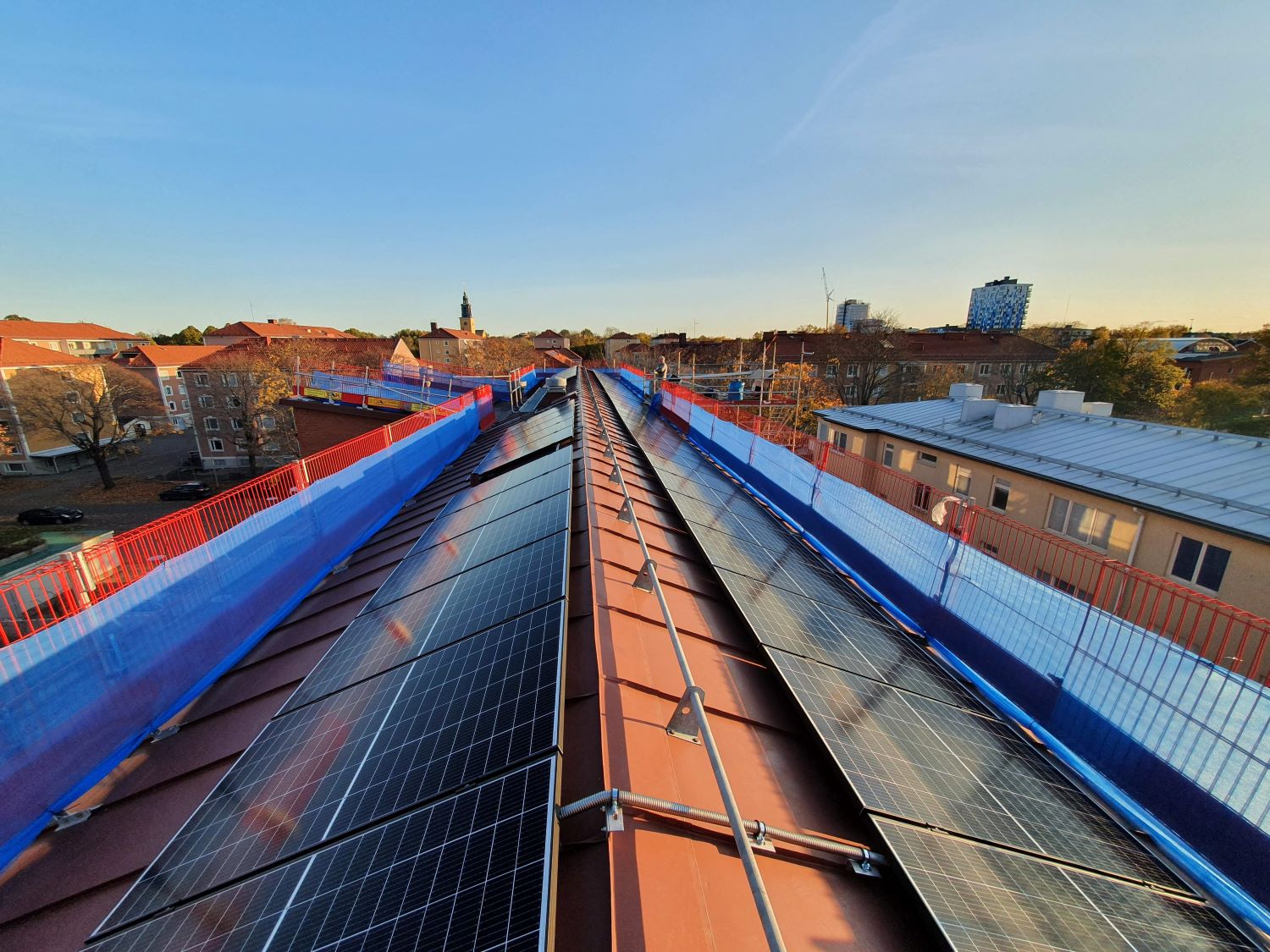 Vy över solceller monterade på ett plåttak, klarblå himmel och natur syns i bakgrunden.